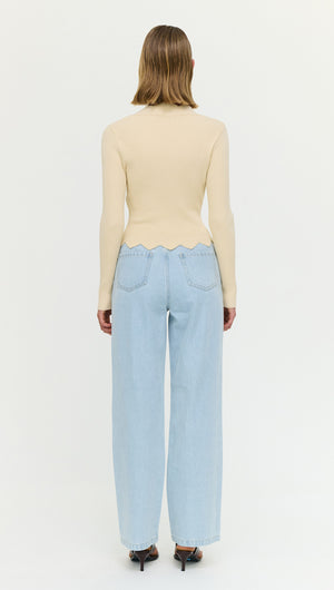 Rear view of a woman wearing an Ornate Button Scallop Neck Cardi in Yellow with light blue high-waisted jeans.