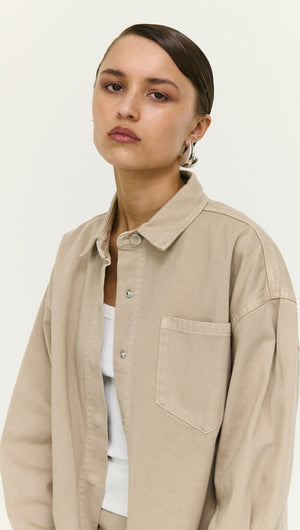 Woman wearing a Stone Wash Relaxed Denim Shacket in beige, styled with a simple white top and hoop earrings.