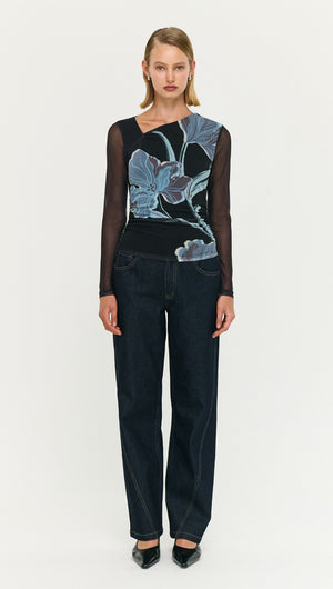 Model wearing a Blue Floral Asymmetric Neck Mesh Top paired with dark jeans, showcasing a stylish contemporary look.