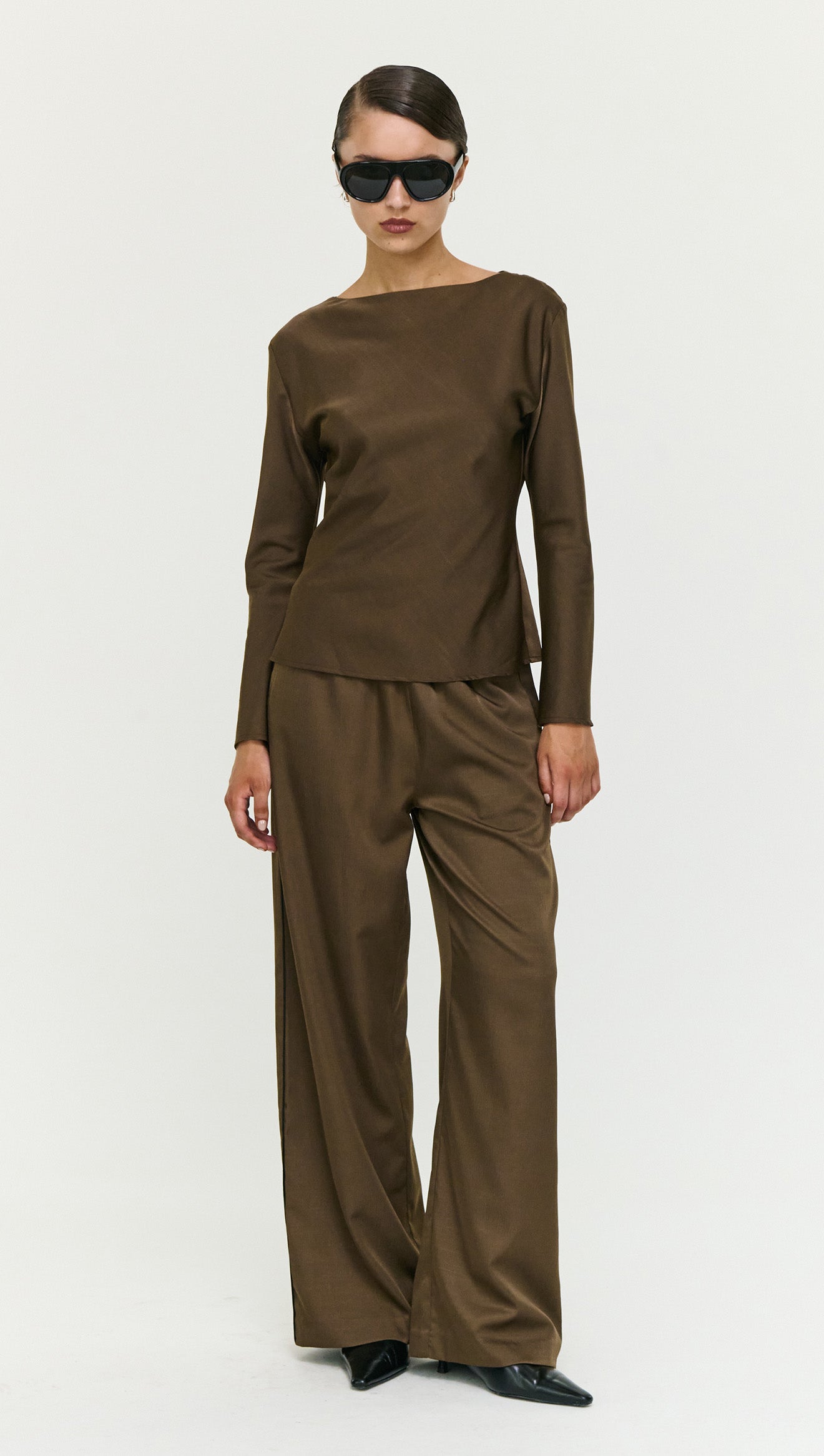 Model wearing Espresso Relaxed Cut Silky Pant with a black textured top and sunglasses, holding a small bag.