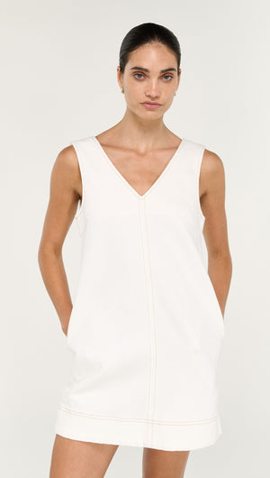 Model wearing a Cotton Denim Mini Shift Dress in White with pockets, featuring a V-neck design on a neutral background.