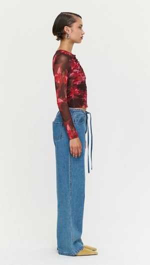Side view of a woman wearing Tie Waist Detail Mid Rise Jeans with a floral long sleeve top.
