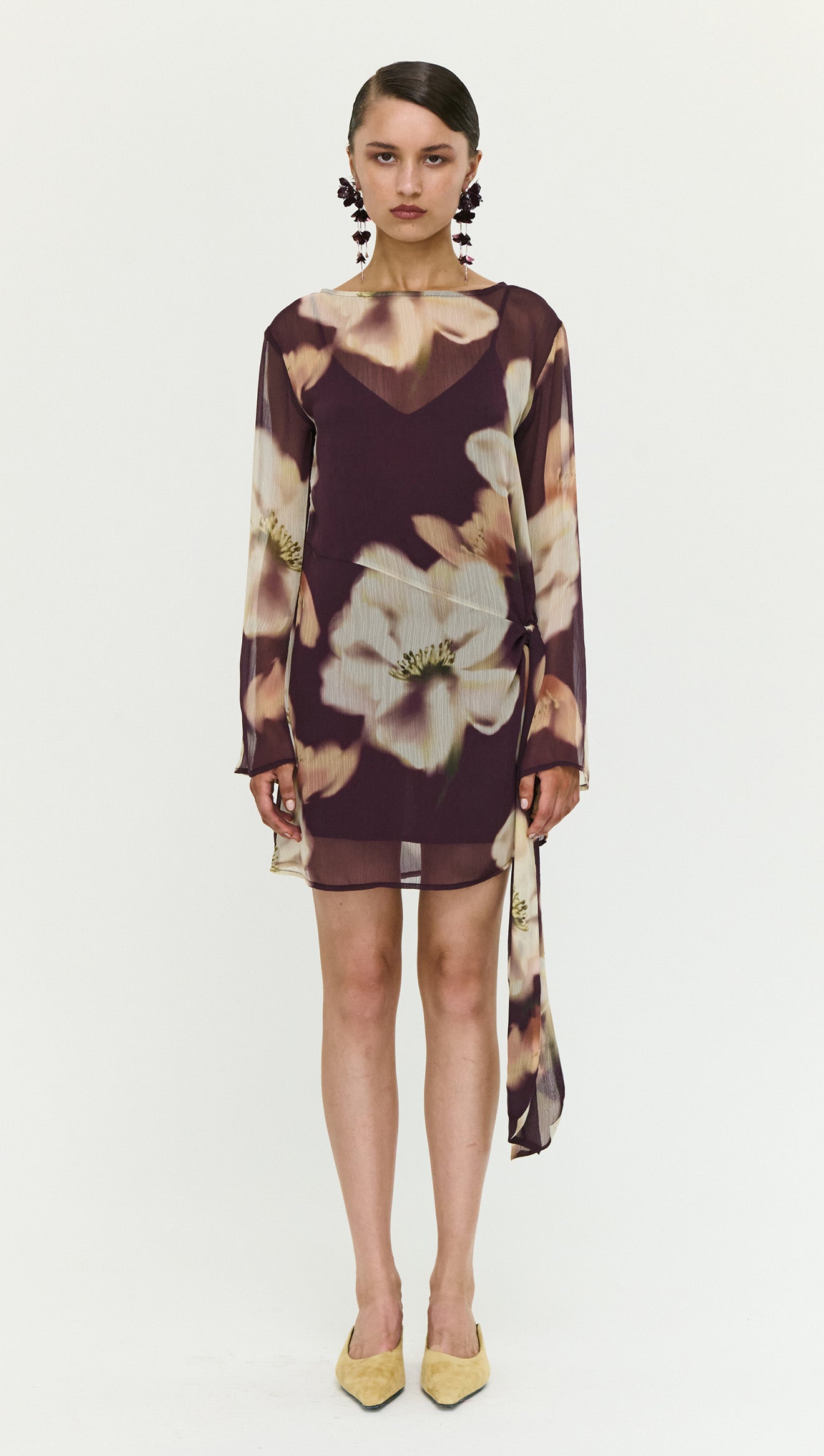 Model wearing a Sheer Floral Mini Dress with Tie Detail, featuring floral patterns and elegant long sleeves.
