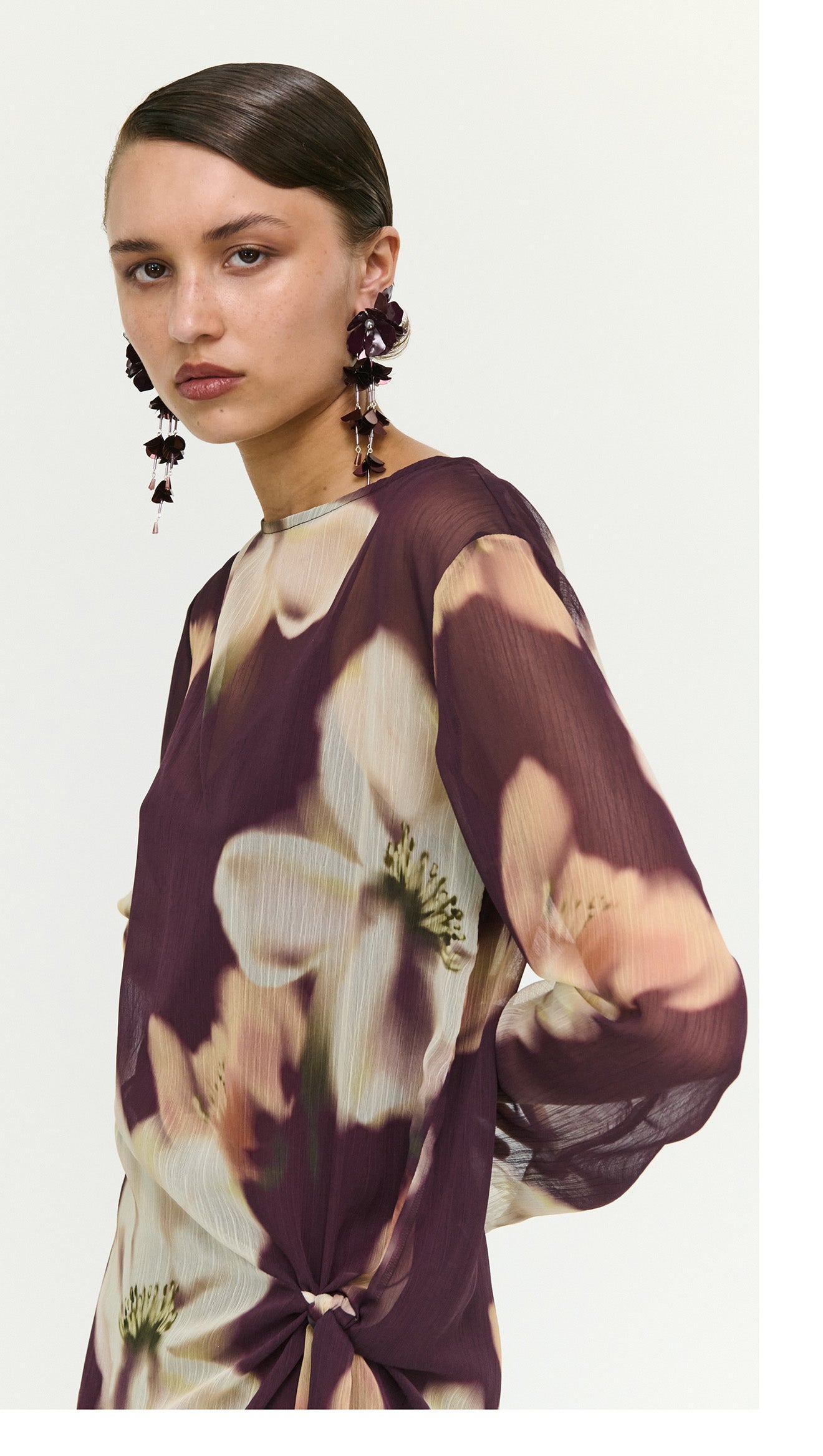 Model wearing a Sheer Floral Mini Dress with Tie Detail, featuring floral patterns and elegant long sleeves.