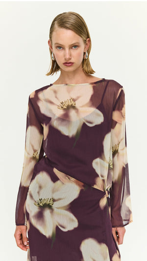 Model wearing a sheer floral maxi dress with tie detail, featuring large white flowers on a deep purple background.