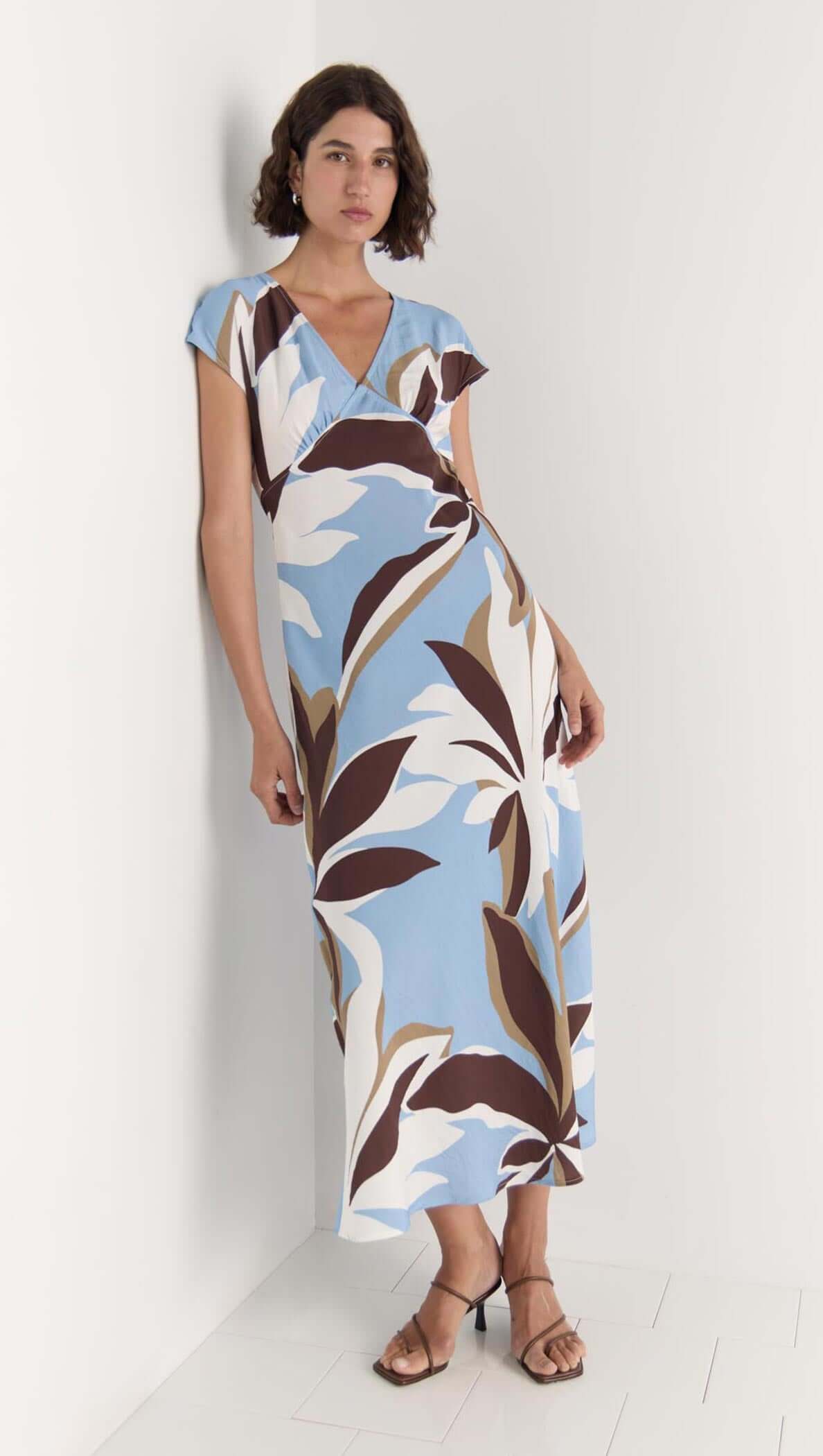 Model wearing Maeve Midi Dress featuring a flattering V-neckline, cap sleeves, and brown, cream, and blue abstract floral print.