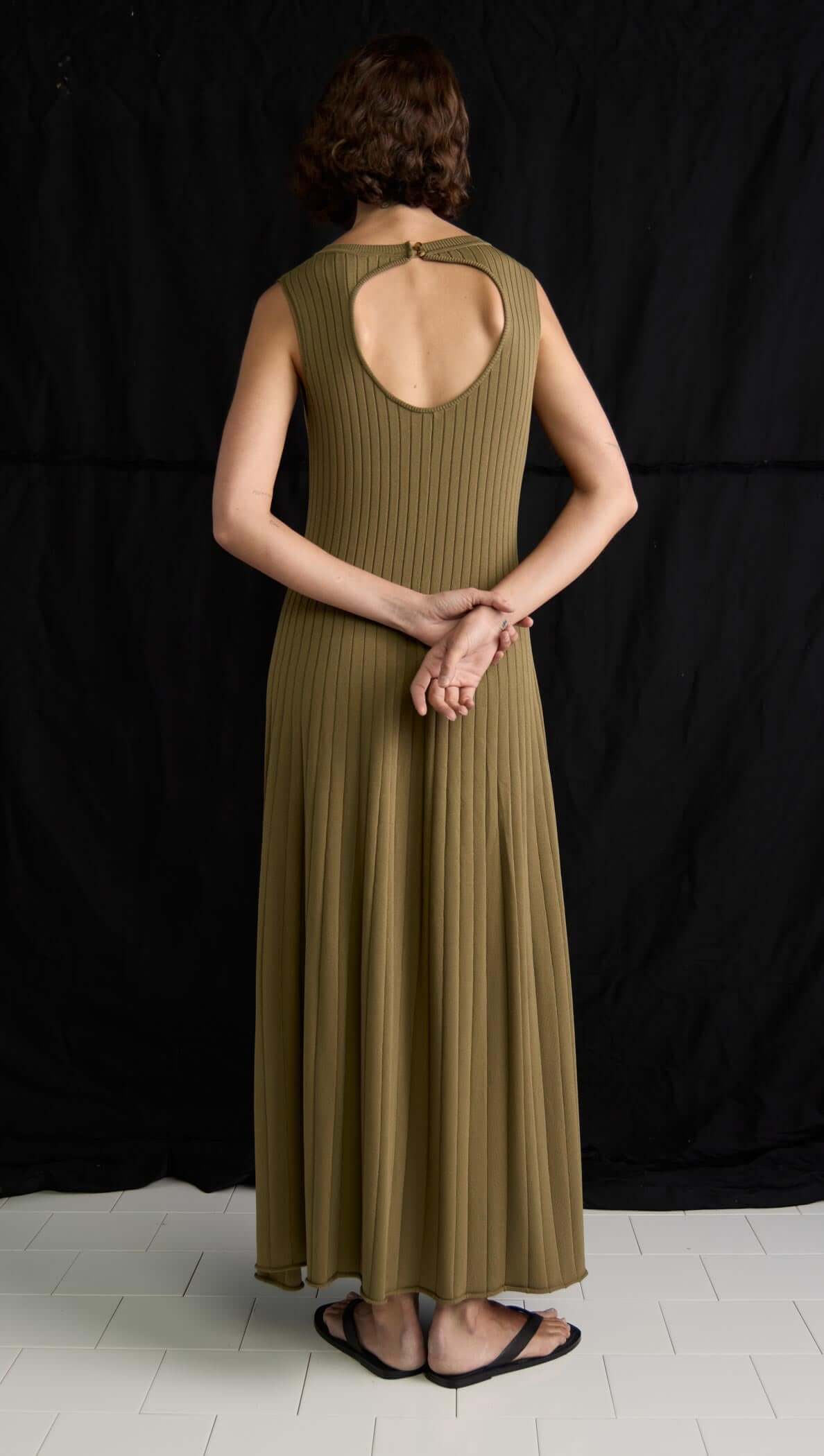 Back view of a woman in an olive-toned ribbed midi dress featuring a keyhole cutout and soft A-line silhouette.