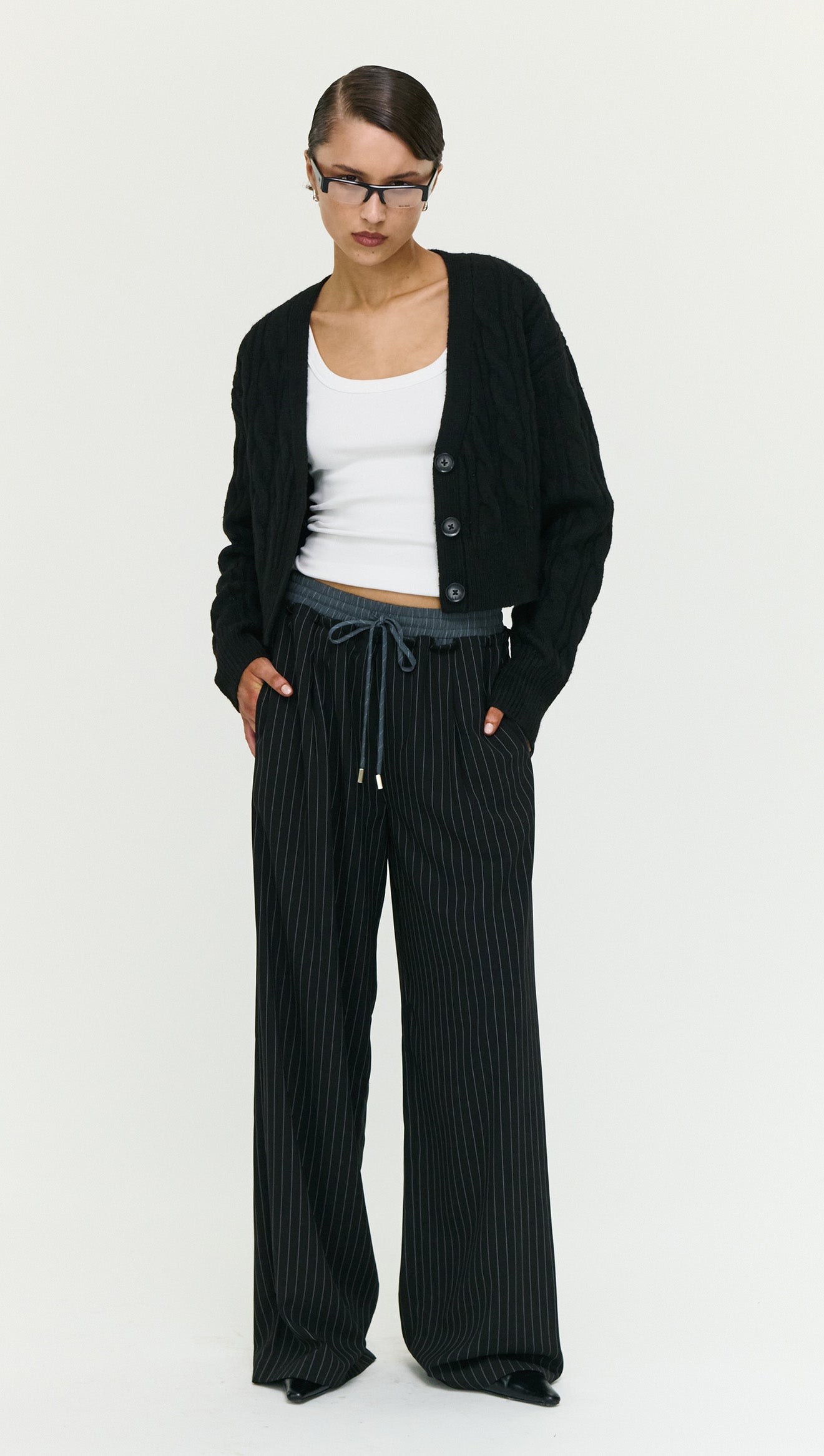 Model wearing a Black Cable Knit Cropped Cardigan over a white top, showcasing a stylish layered look.
