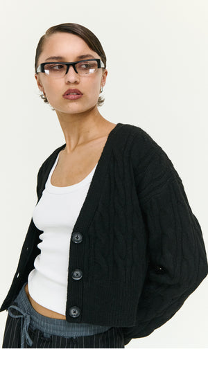 Model wearing a Black Cable Knit Cropped Cardigan over a white top, showcasing a stylish layered look.