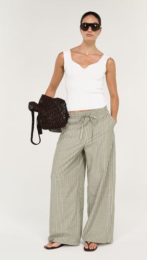 Model wearing Khaki Stripe Relaxed Cotton Pant with a white top and sunglasses, holding a dark bag.