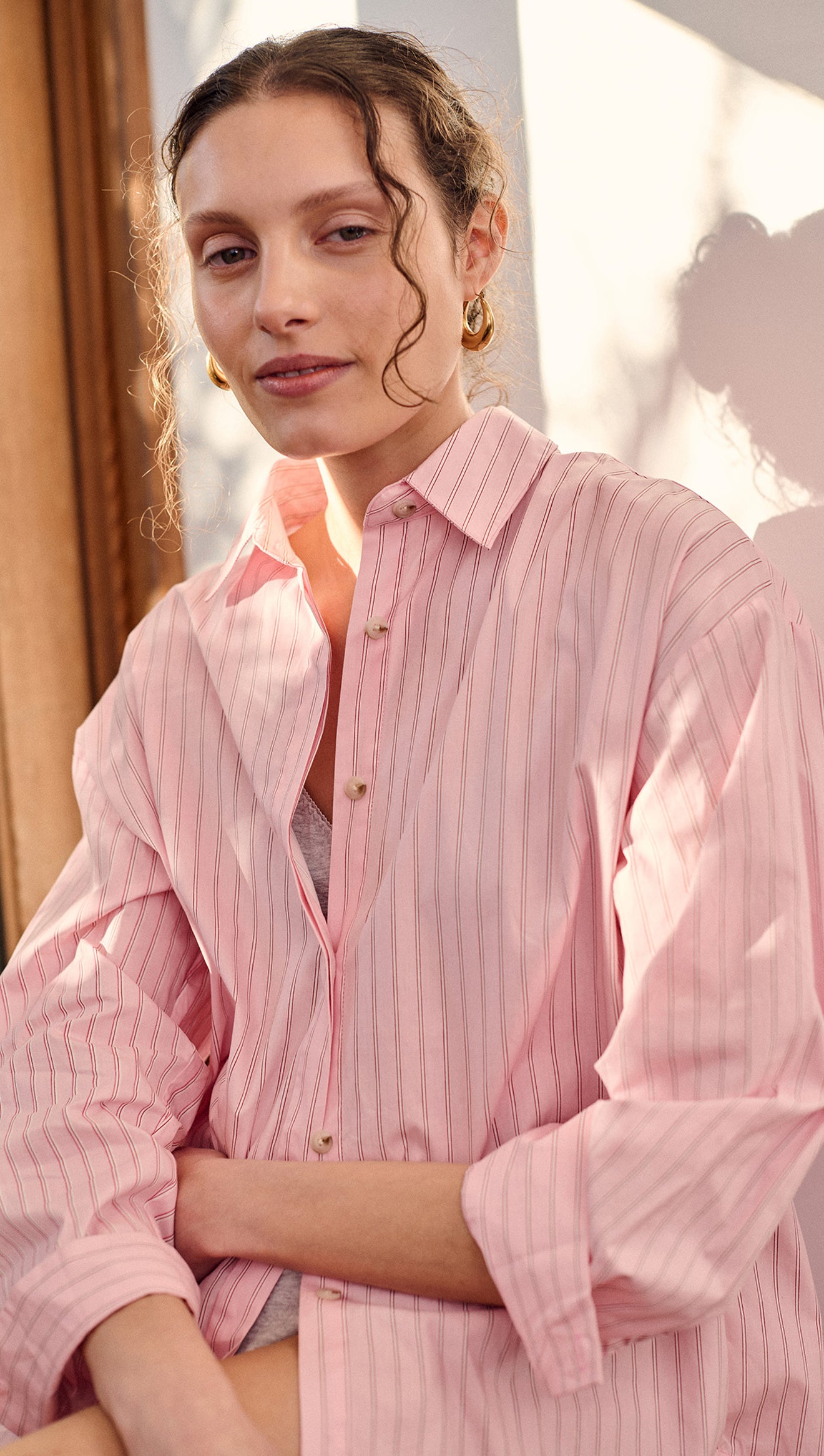 Woman wearing an Oversized Cotton Shirt with Back Button Detail in pink stripes, showcasing a relaxed fit and unique design.