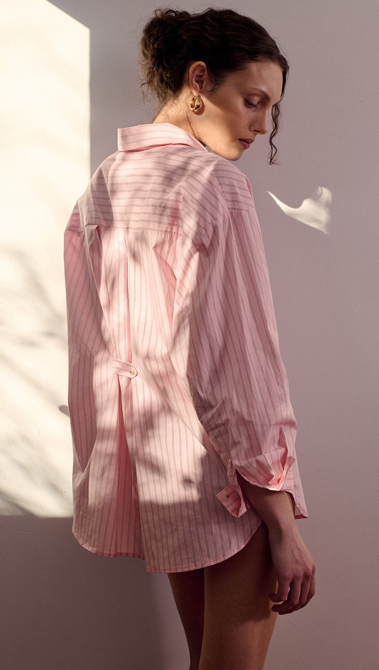 Woman wearing an Oversized Cotton Shirt with Back Button Detail in pink stripes, showcasing a relaxed fit and unique design.