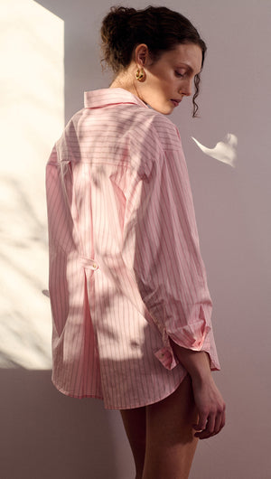 Woman wearing an Oversized Cotton Shirt with Back Button Detail in pink stripes, showcasing a relaxed fit and unique design.