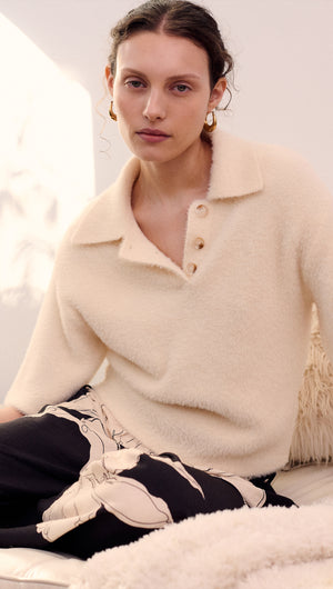 Model wearing a Fluffy Knit Polo Top in Cream, featuring button details and a relaxed fit, styled with patterned pants.