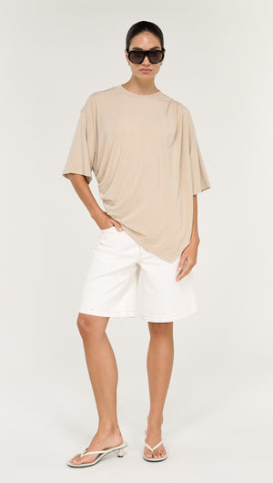 Model wearing Asymmetric Draped Oversize Tee in Beige with white shorts and sunglasses.
