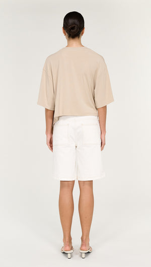Asymmetric Draped Oversize Tee in Beige worn from the back with white shorts and sandals.