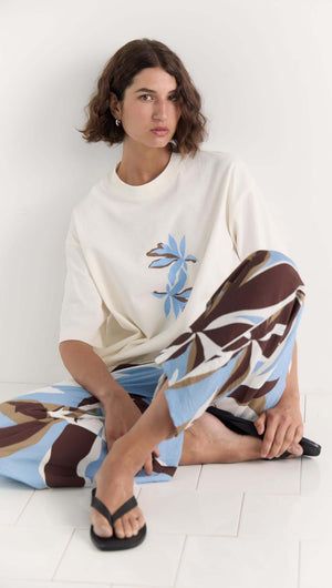 Model wearing Mae Graphic Tee with cream base, blue and brown floral print, paired with relaxed pants.