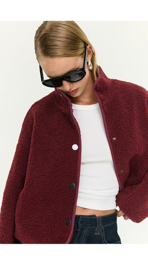 Model wearing a Burgundy High Neck Cropped Sherpa Jacket, styled with sunglasses and a white top, perfect for cool weather.