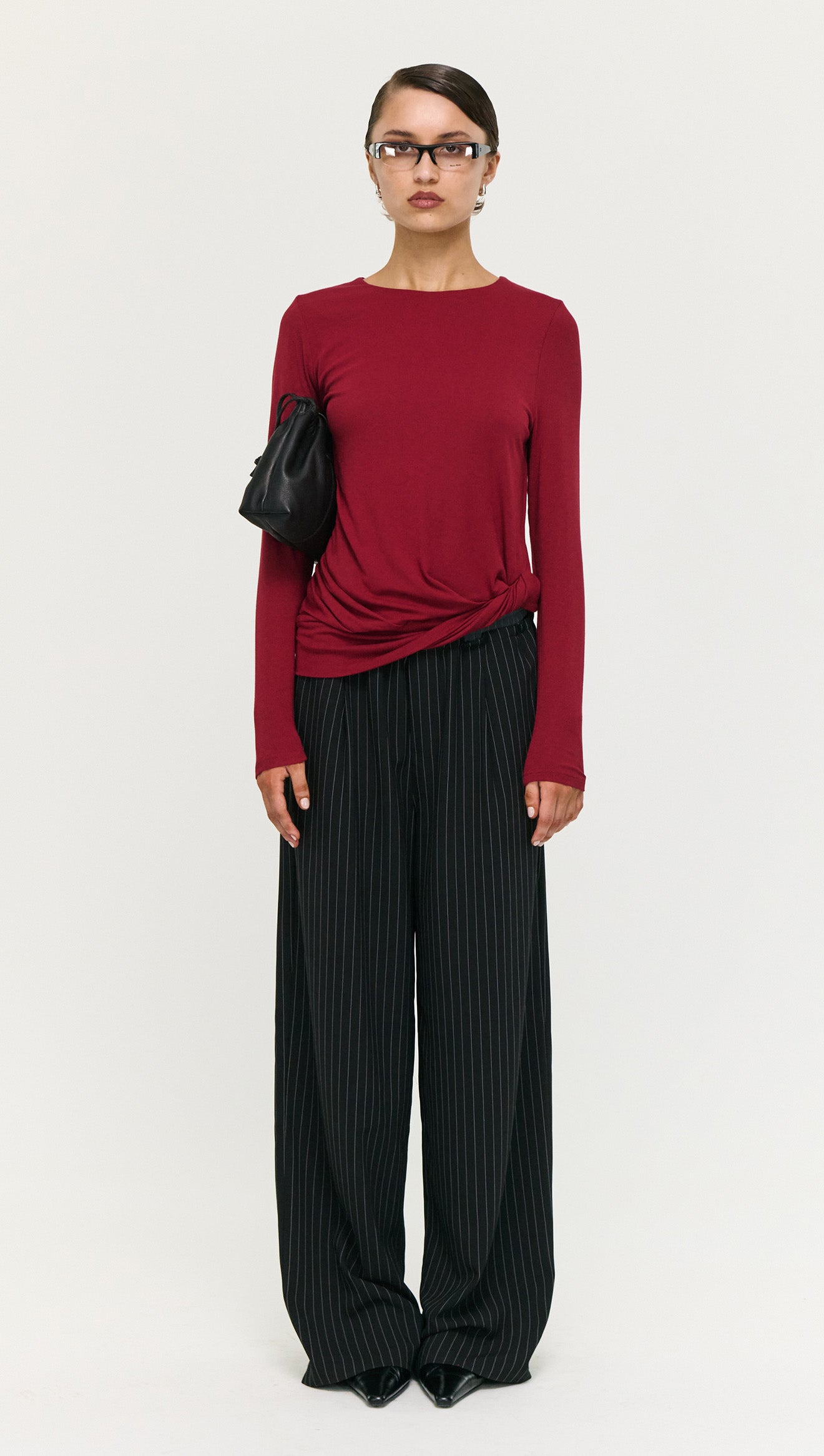 Model wearing a Long Sleeve Jersey Twist Top in Merlot paired with black striped wide-leg pants.