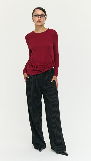 Model wearing Long Sleeve Jersey Twist Top in Merlot with striped pants against a neutral background.
