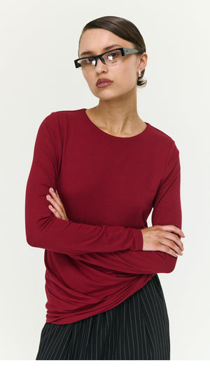 Model wearing Long Sleeve Jersey Twist Top in Merlot, paired with striped pants, showcasing a trendy layered look.