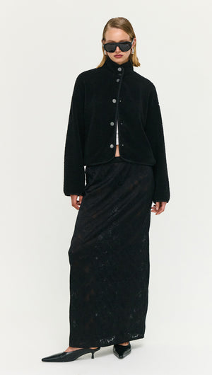 Model wearing a Black High Neck Cropped Sherpa Jacket paired with a long black skirt and sunglasses.