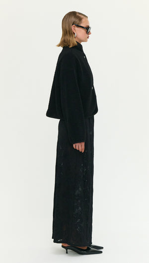 Side view of a model wearing a Black High Neck Cropped Sherpa Jacket styled with a long black skirt.