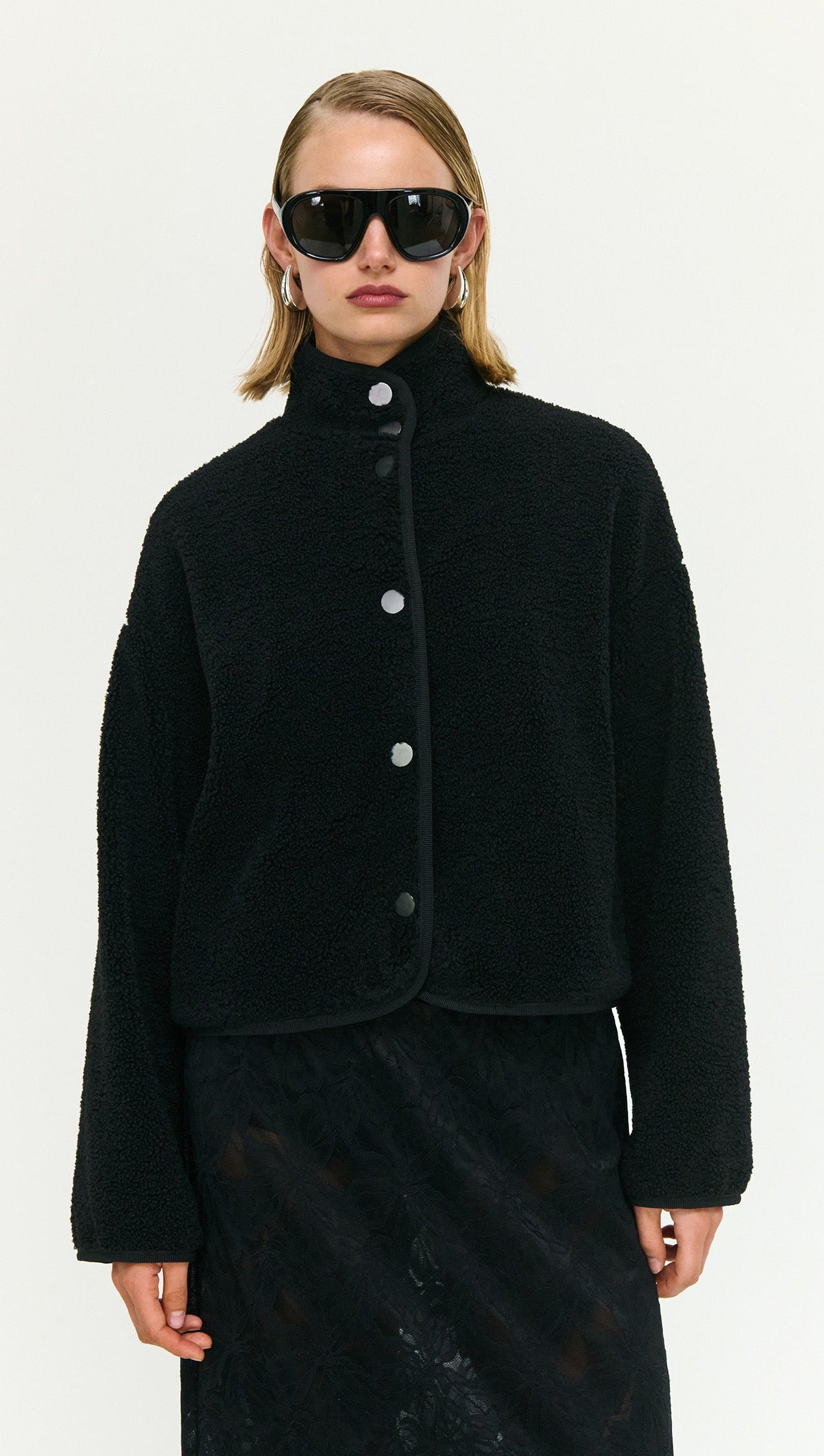 Model wearing a Black High Neck Cropped Sherpa Jacket with stylish sunglasses, showcasing cozy winter fashion.