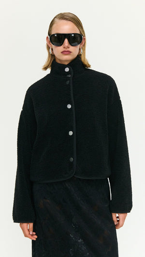 Model wearing a Black High Neck Cropped Sherpa Jacket with stylish sunglasses, showcasing cozy winter fashion.