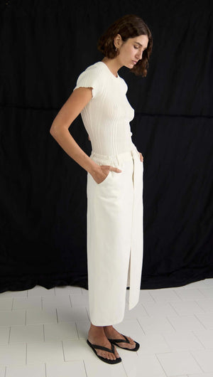 Model wearing the Emmie Denim Midi Skirt in off-white, featuring a high waist and front split, styled with a ribbed top.