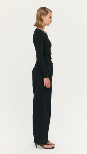Model wearing Black Soft Jersey Twist Neck Top from the side, showcasing a sleek silhouette and soft stretch fabric.