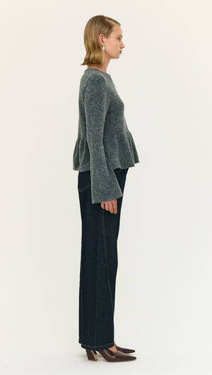 Model wearing a Soft Knit Peplum Top with Flute Sleeve paired with dark jeans, showcasing a side view.