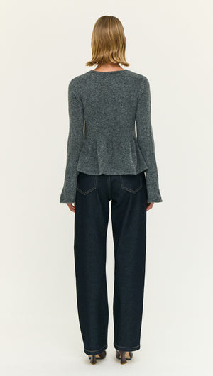 Back view of a model wearing a Soft Knit Peplum Top with Flute Sleeve paired with dark blue jeans.