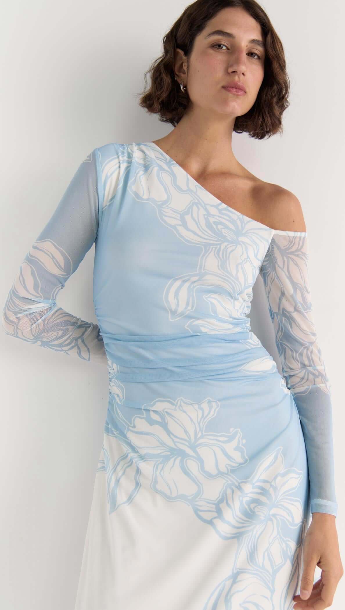 Model wearing the Aurora Mesh Midi Dress in sky blue floral mesh with one-shoulder design and side ruching.