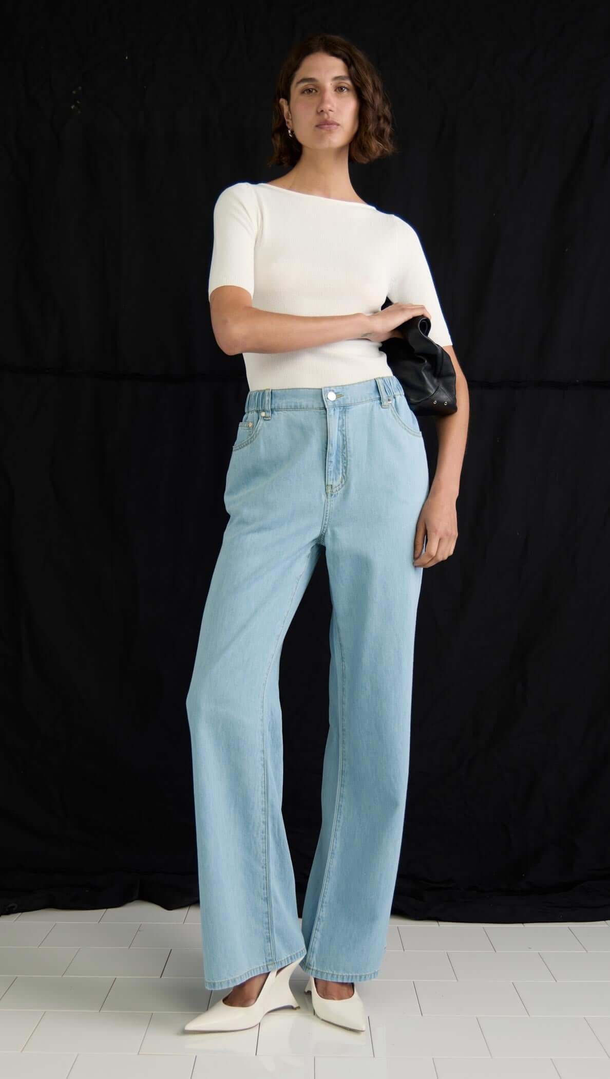 Model wearing light chambray blue Amelia Chambray Jeans with a fitted white top and black handbag.