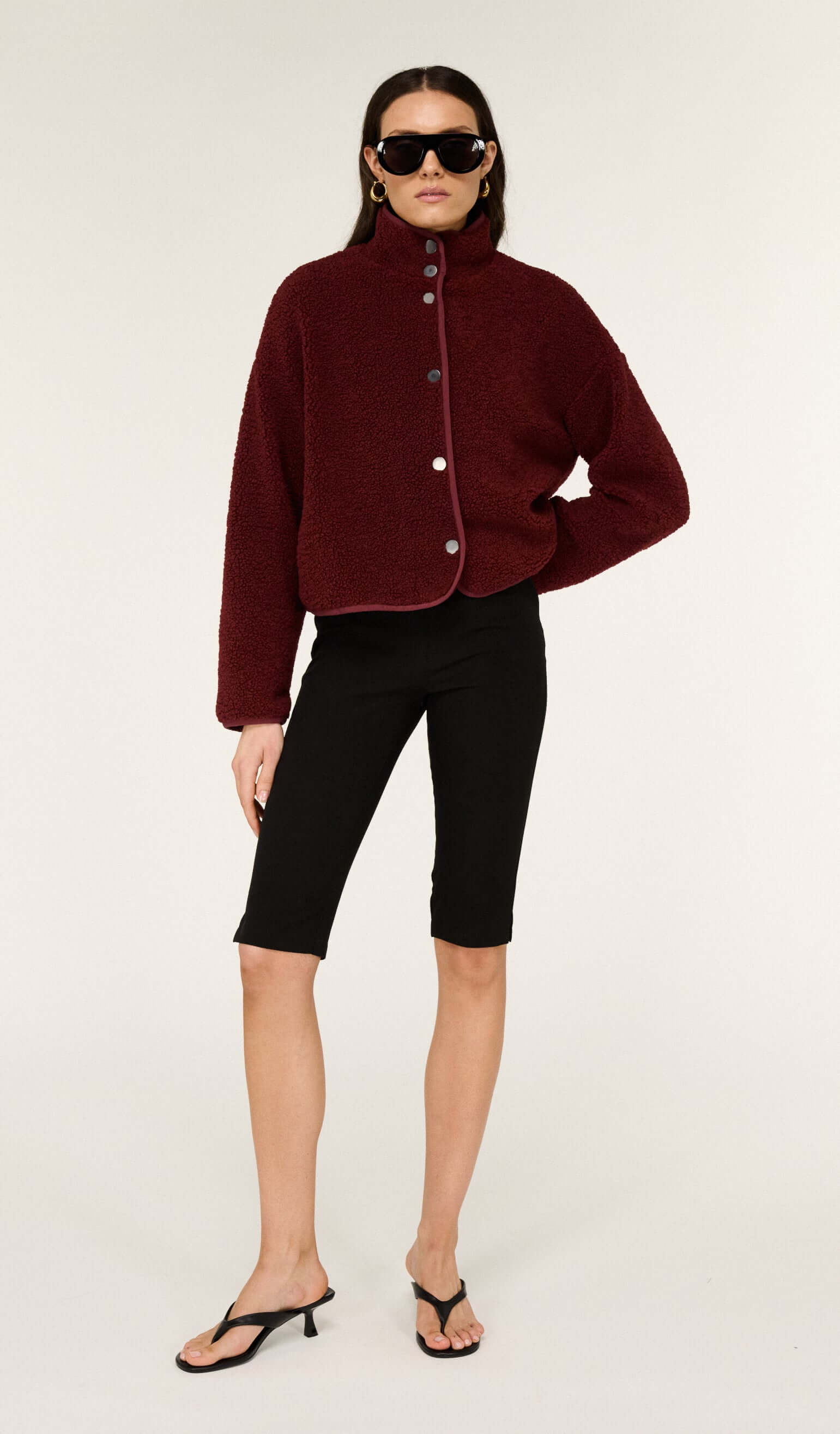 Model wearing Mid Rise Capri Pants in Black with a burgundy jacket and sunglasses, showcasing a trendy casual outfit.