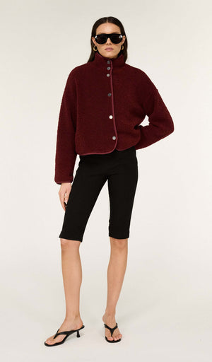 Model wearing Mid Rise Capri Pants in Black with a burgundy jacket and sunglasses, showcasing a trendy casual outfit.