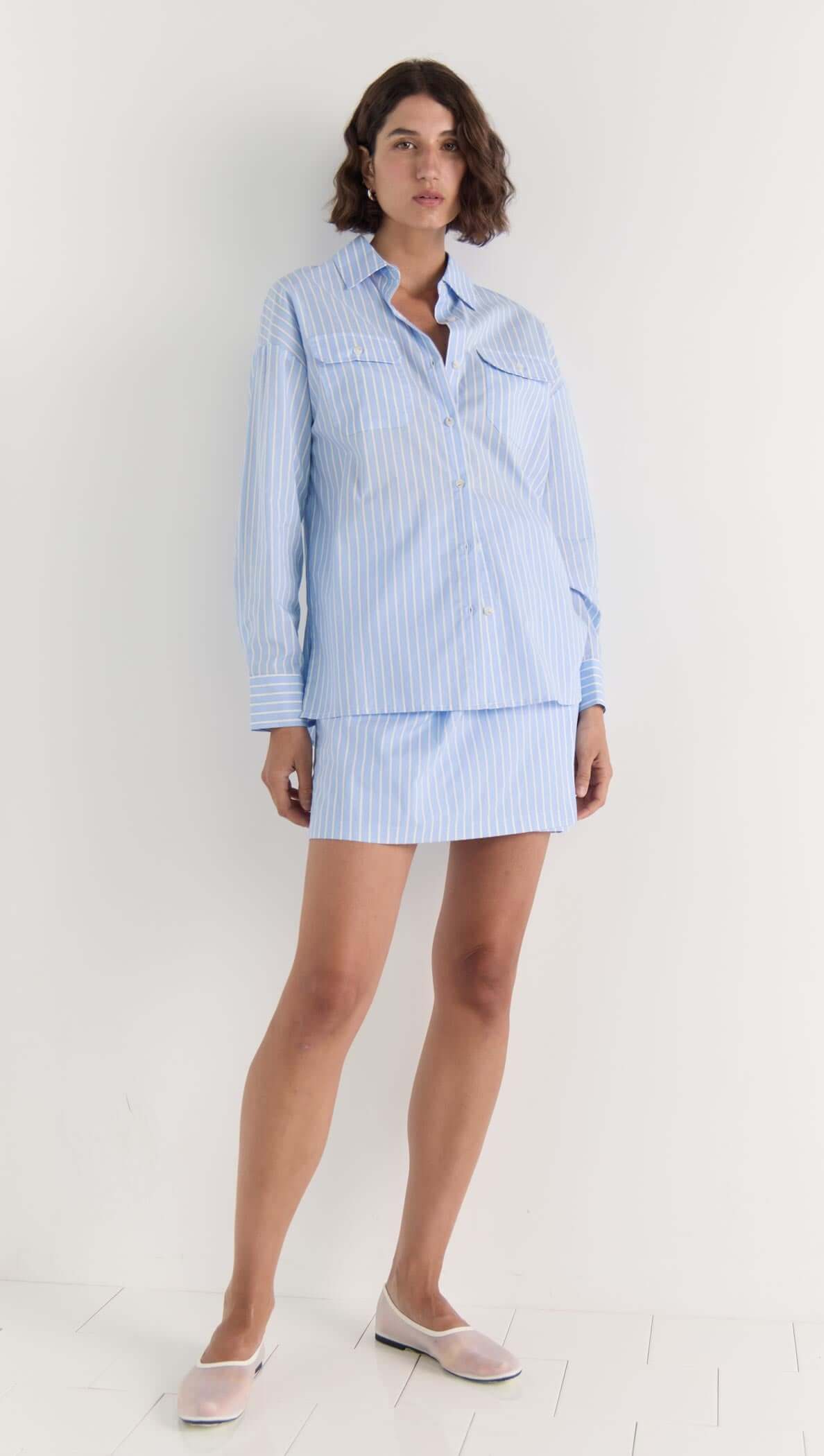 Model wearing the Ayra Wrap Mini Skirt and matching blue striped shirt, showcasing a chic warm-weather outfit.