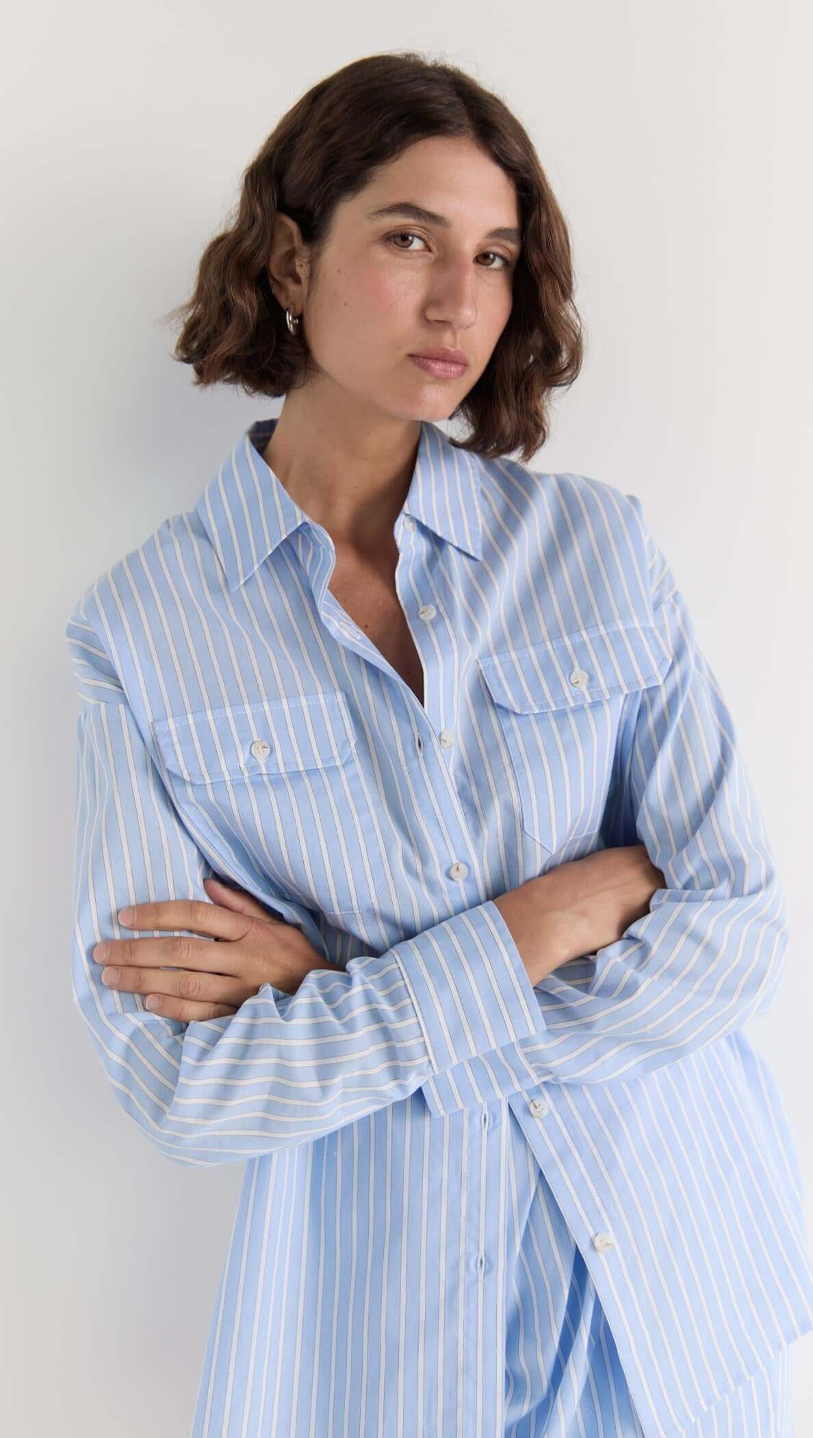 Model wearing the Ayra Pinstripe Shirt in blue stripe, featuring a relaxed fit, button-up front, and chest pockets.
