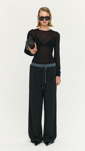 Model wearing Pinstripe Relaxed Drawstring Pants paired with a sheer black top and sunglasses, holding a small black bag.