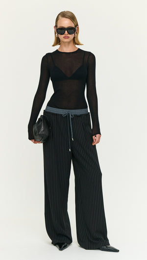 Model wearing Pinstripe Relaxed Drawstring Pants with a black sheer long sleeve top and sunglasses.