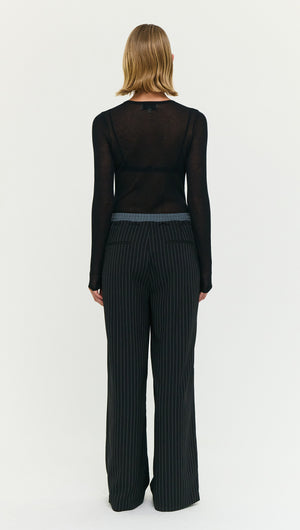 Back view of a woman wearing Pinstripe Relaxed Drawstring Pants with a sheer black long-sleeve top.