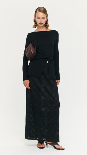 Model wearing a Black Boat Neck Twist Knit Top paired with a long black skirt and accessories, exuding modern style.