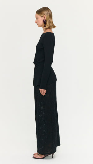 Model wearing a Black Boat Neck Twist Knit Top side view, paired with a long black skirt.