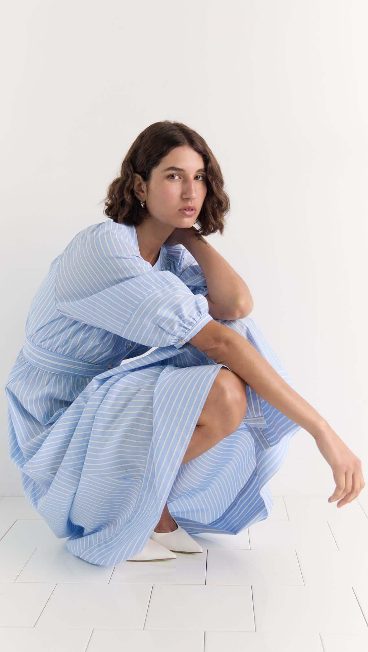 Model wearing the Myra Midi Dress with soft blue pinstripes, voluminous puff sleeves, and an empire waist.
