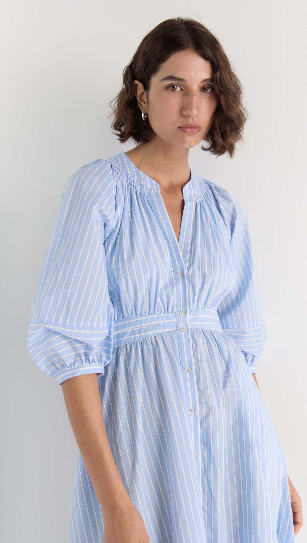 Model wearing the Myra Midi Dress with soft blue pinstripes, puff sleeves, and a button-down front.