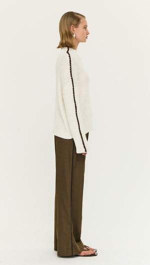 Model wearing a Blanket Stitch Detail High Neck Jumper paired with wide-leg pants, showcasing a side profile view.