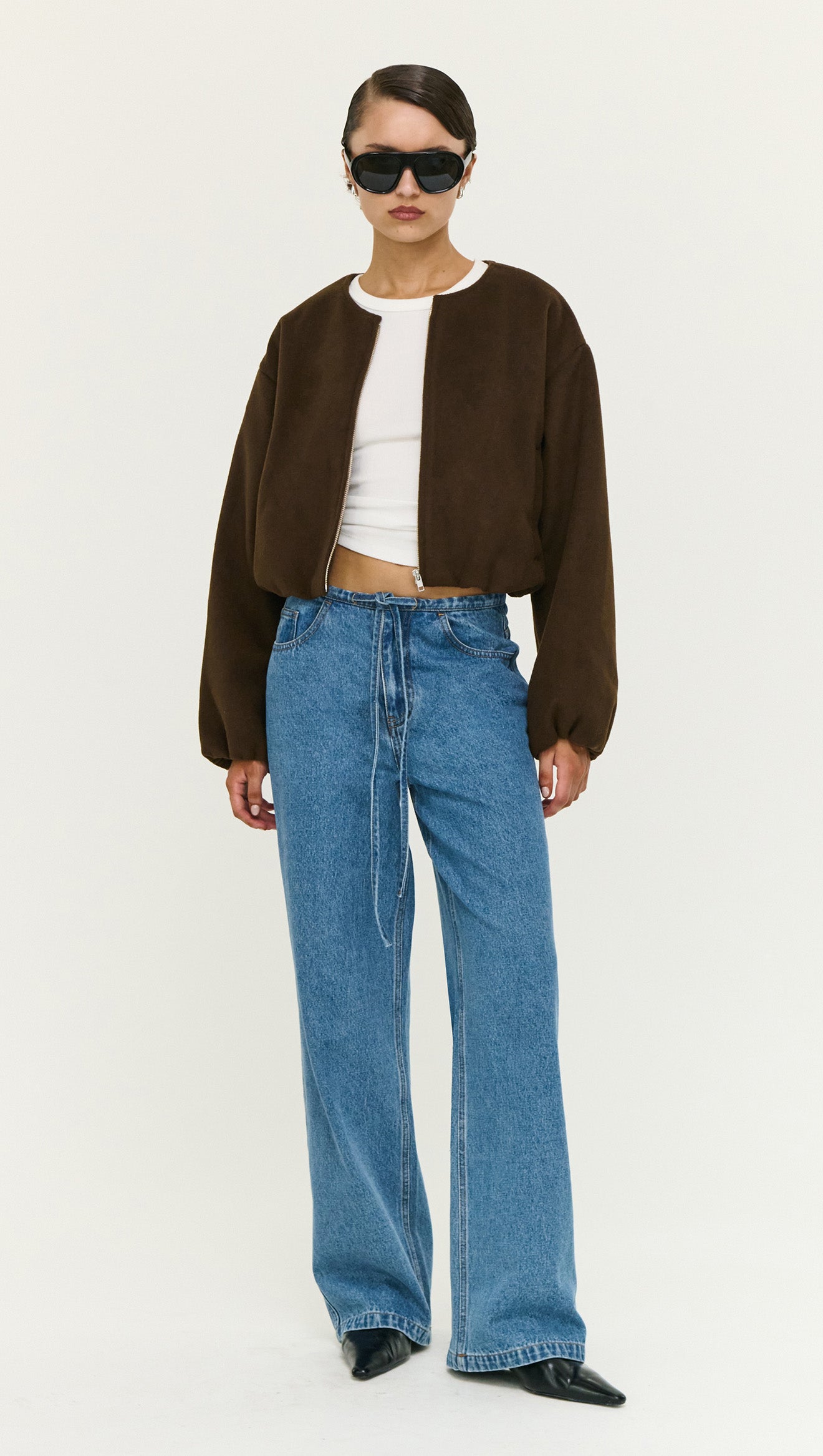 Model wearing a Soft Brushed Cropped Bomber Jacket with oversized jeans and sunglasses, showcasing modern outerwear style.