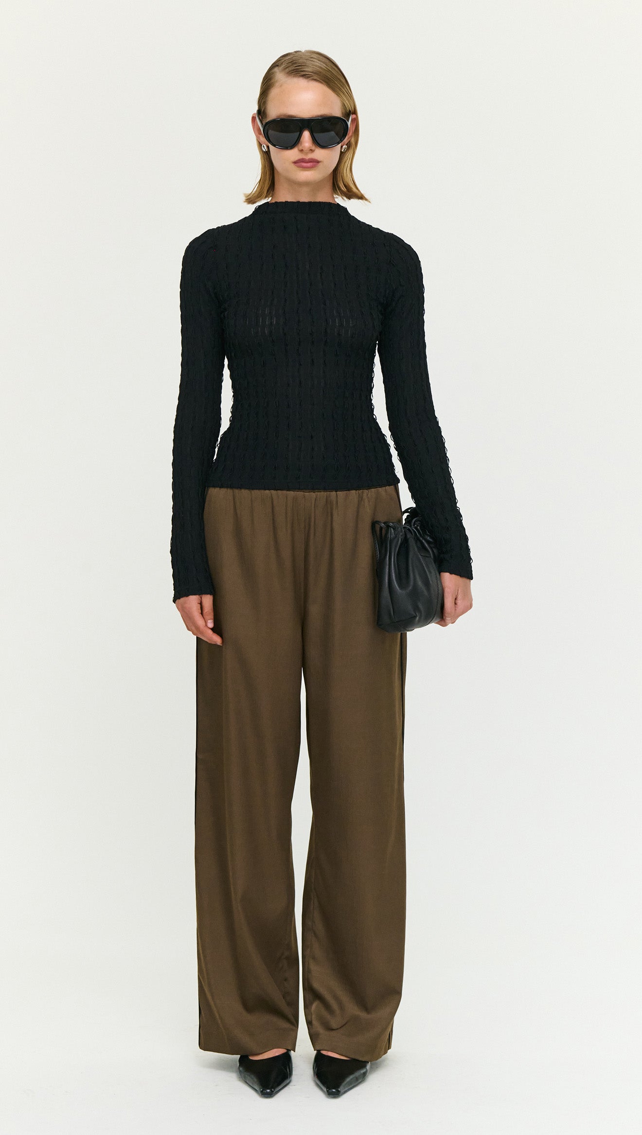 Model wearing Espresso Relaxed Cut Silky Pant with a black textured top and sunglasses, holding a small bag.