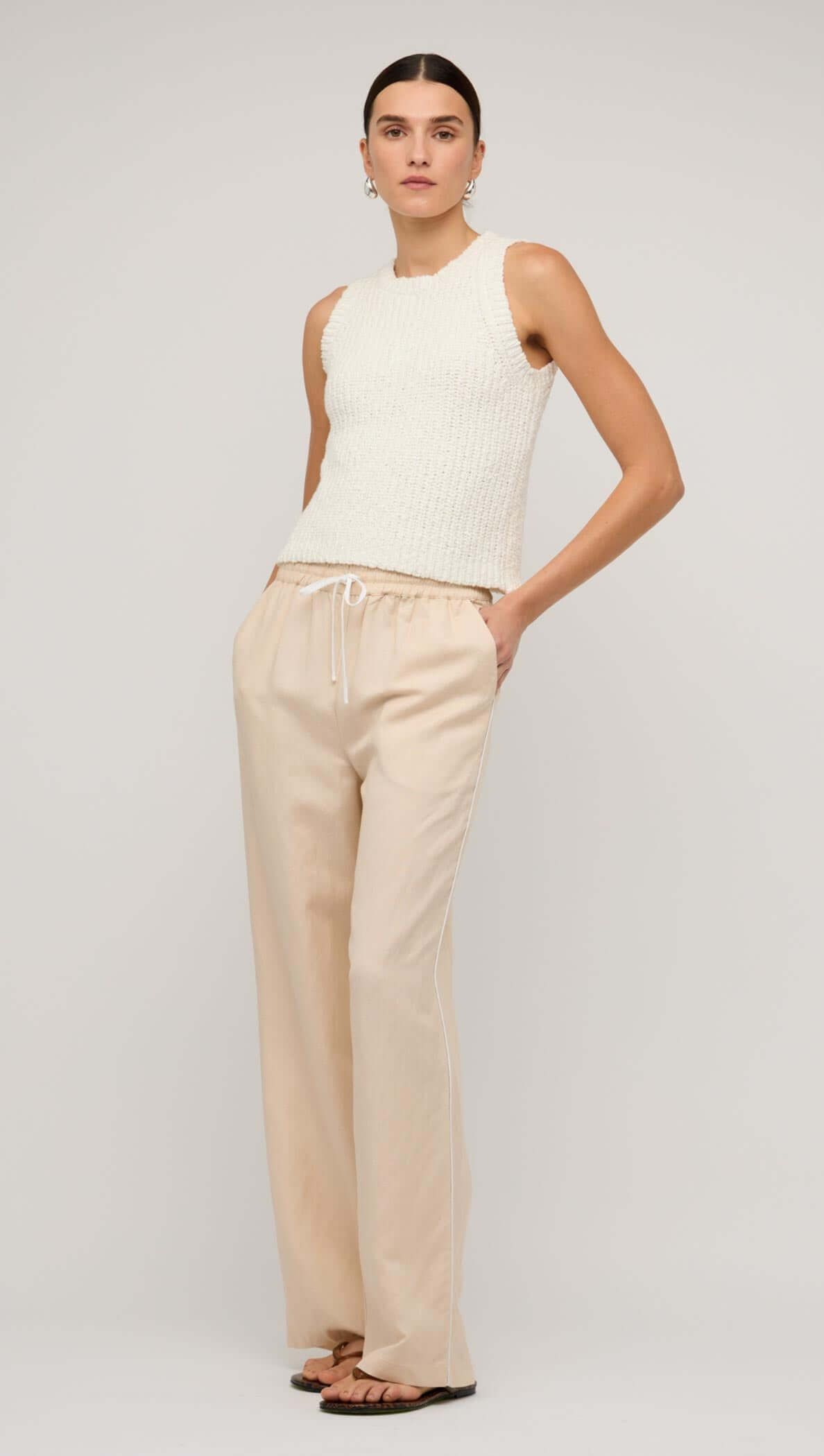 Model wearing beige relaxed linen wide-leg pants paired with a knitted tank top, showcasing casual yet stylish summer fashion.